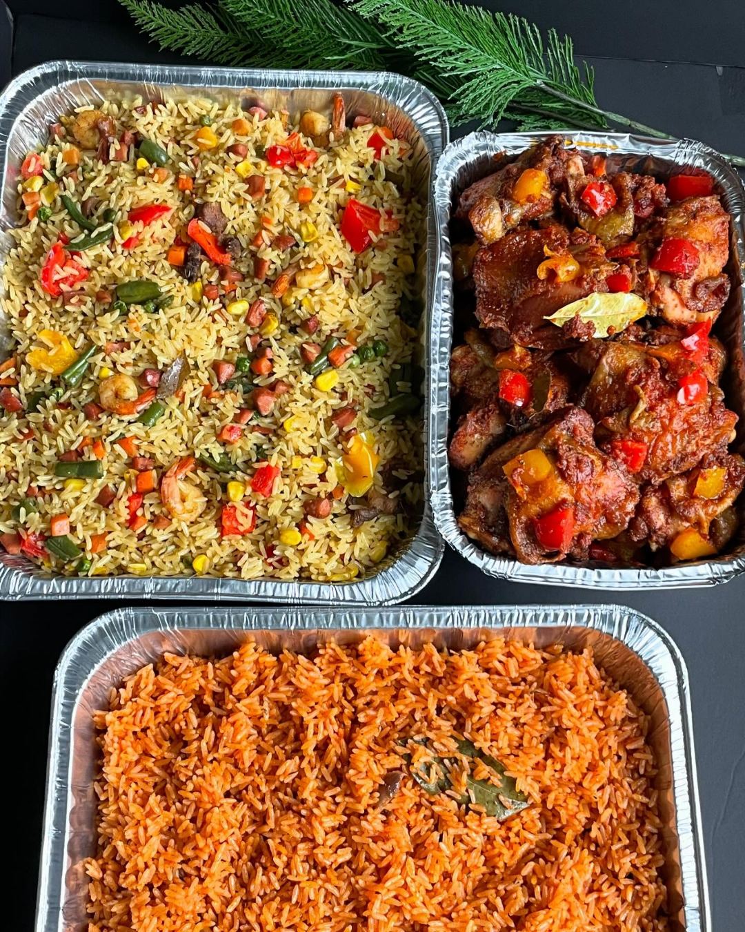 Foil catering trays of fried rice, jollof rice and peppered chicken